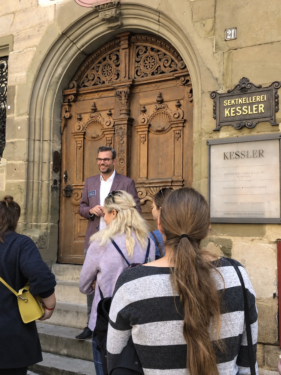 Andreas Schnug lächelt bei der Begrüßung einer Gästegruppe vor der großen Holztür der Sektkellerei Kessler